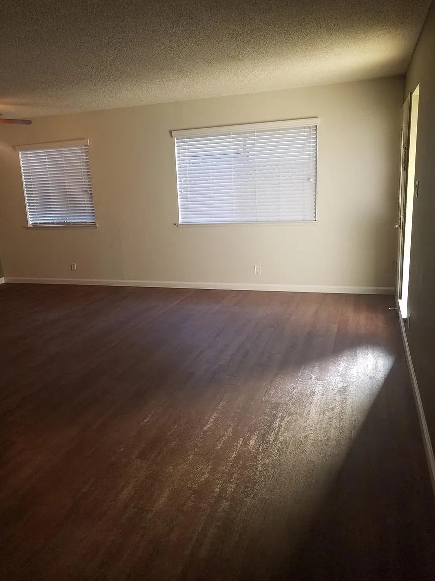 A room with wooden floors and two windows with blinds.